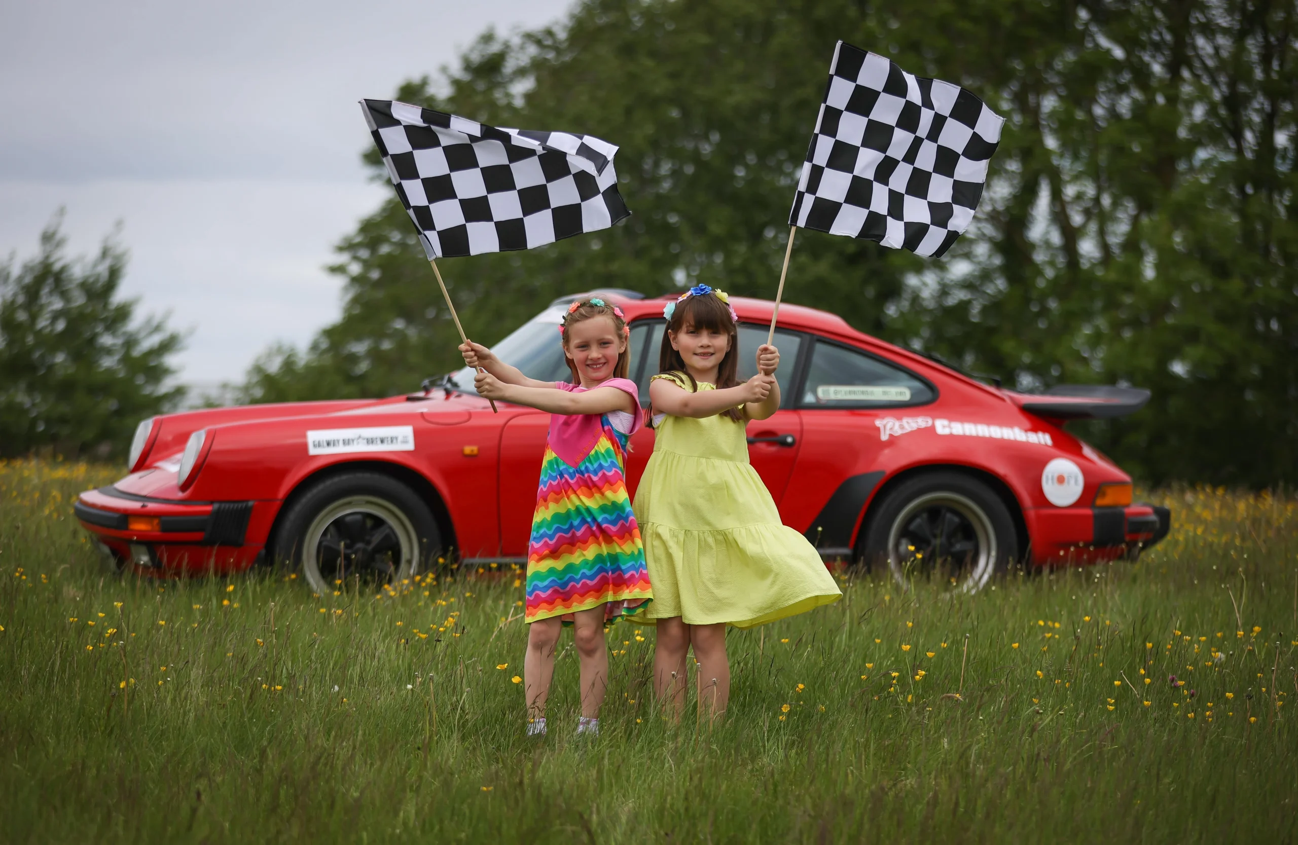 two girls waving flags in front of retro car
