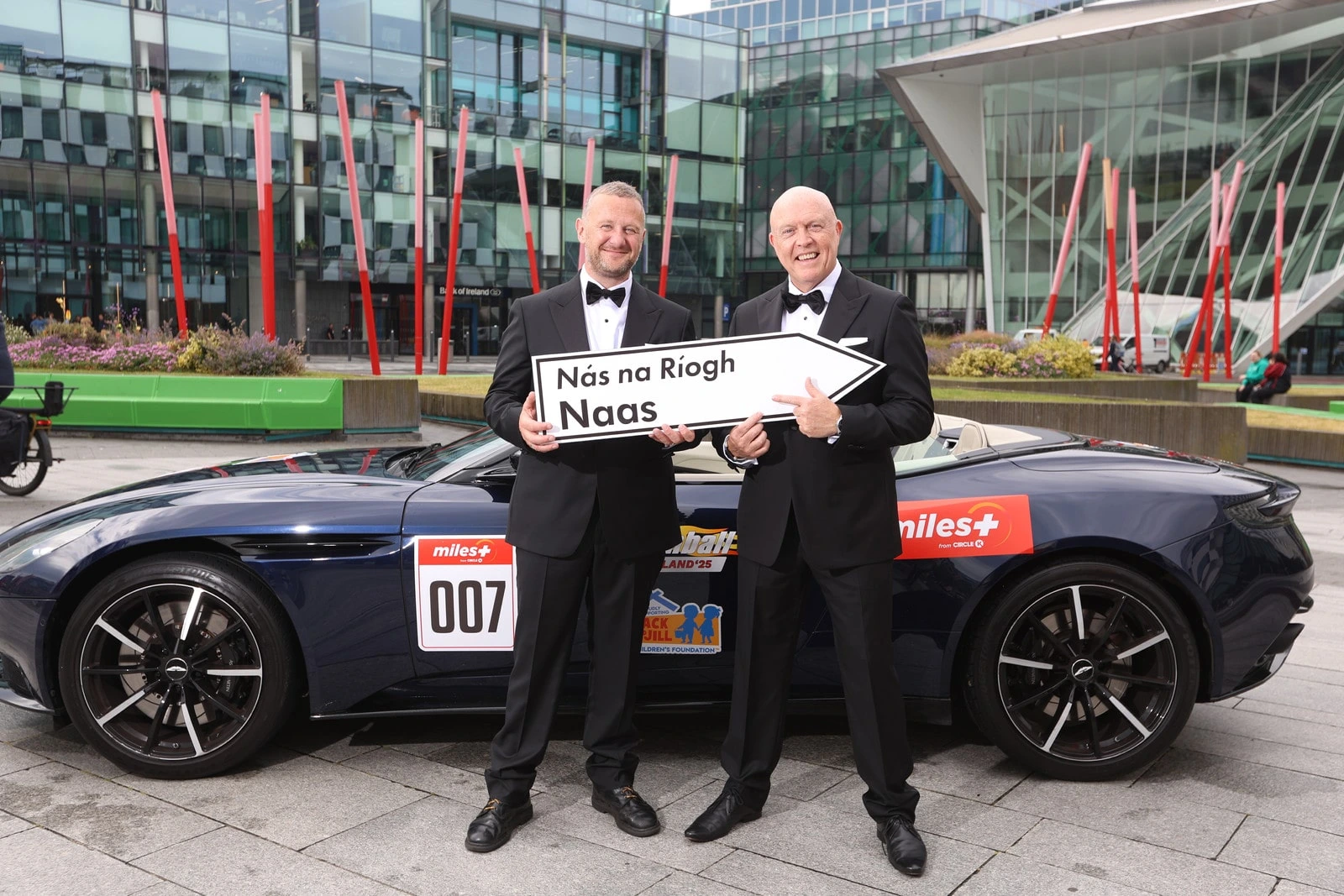 Radio Nova’s PJ Gallagher and Jim McCabe with Naas road sign standing in front of Aston Martin DB11