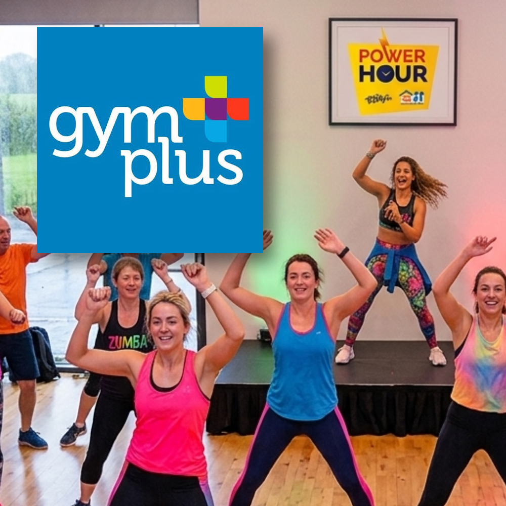 Gym Plus Ireland A group of people participating in a fitness class inside a studio, with a framed "Power Hour" sign on the wall and a blue logo overlay for "gym plus".