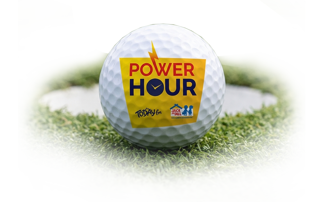 A white golf ball featuring the Power Hour logo with Today FM and Jack & Jill branding, resting near a golf hole on a green turf.