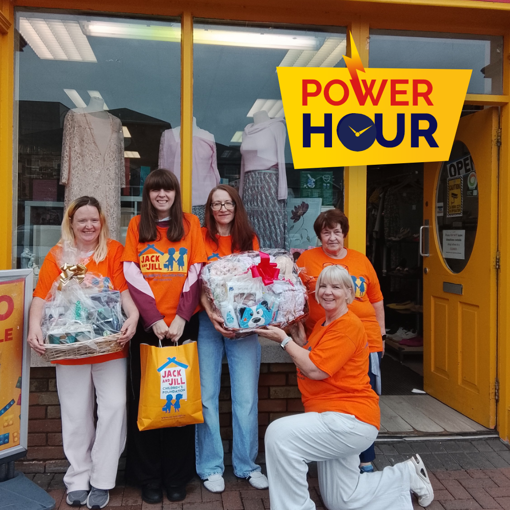 Power Hour Newbridge Five Jack and Jill staff members in orange t-shirts holding gift hampers and a branded bag outside a storefront, featuring the Power Hour logo.
