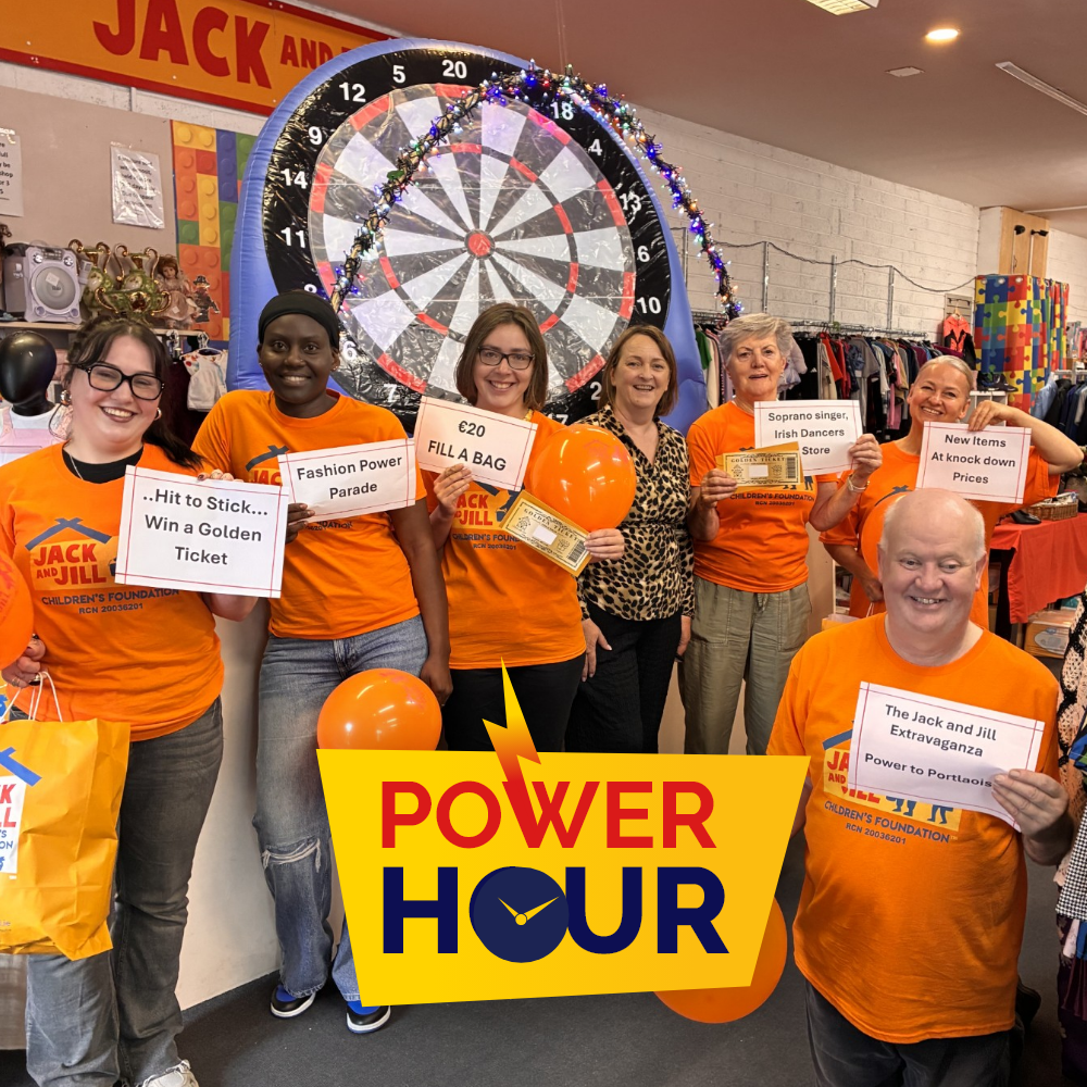 Power Hour Portlaoise A team of Jack and Jill staff members inside a store holding promotional signs, balloons, and golden tickets in front of a large inflatable dartboard, featuring the Power Hour logo.