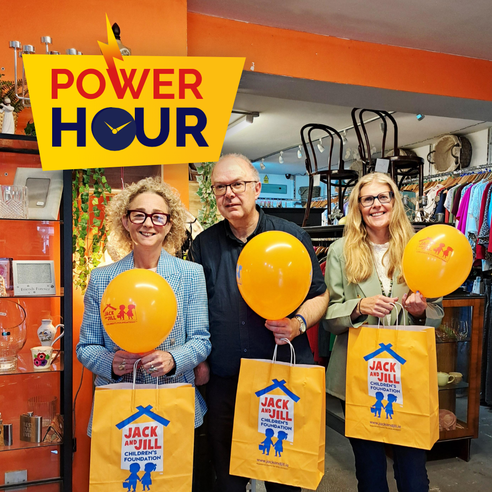 Power Hour Wicklow Three Jack and Jill charity boutique team members holding orange balloons and yellow branded shopping bags inside the store, featuring the Power Hour logo.