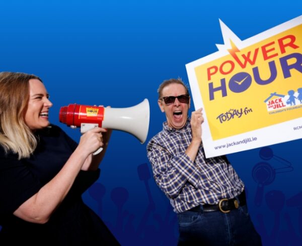 A woman speaking through a megaphone at a man holding a large Power Hour promotional sign for Today FM and the Jack and Jill Children's Foundation.