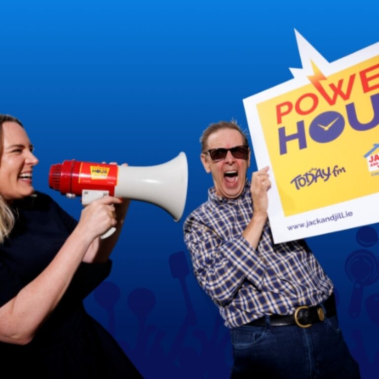 A woman speaking through a megaphone at a man holding a large Power Hour promotional sign for Today FM and the Jack and Jill Children's Foundation.