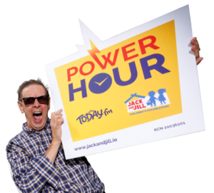 Today FM presenter Ian Dempsey wears sunglasses and a plaid shirt, shouting enthusiastically while holding a large sign promoting the Power Hour for the Jack and Jill Children's Foundation.